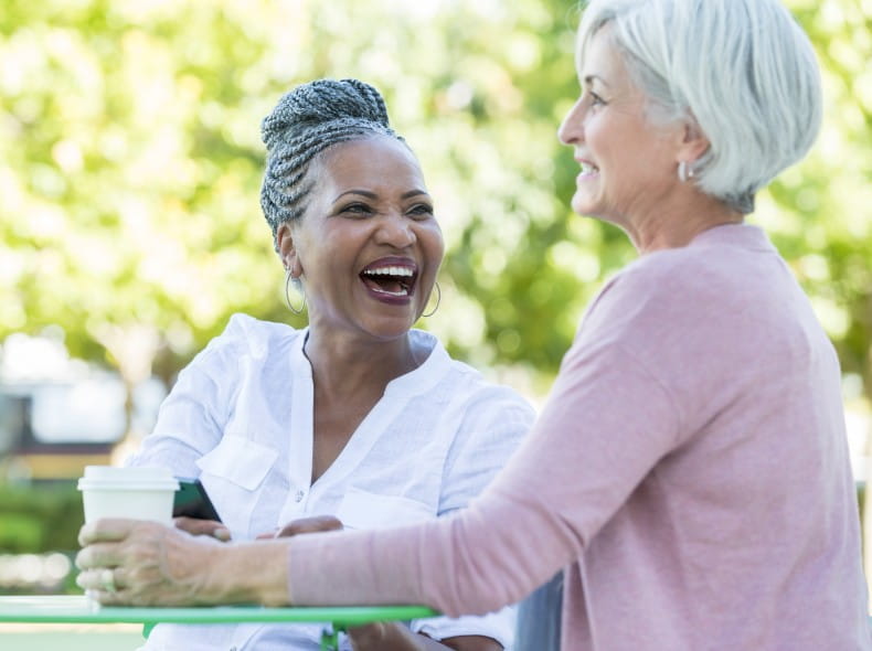 Two older woman sitting outside smiling and laughing while talking