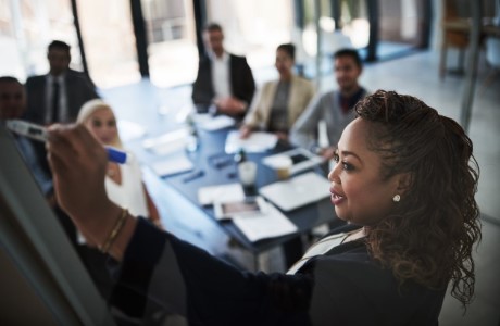 an image of a women writing on a whiteboard during a meeting.