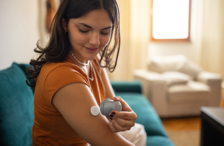 Young diabetic patient teenage woman using applicator to attach glucose sensor on arm.